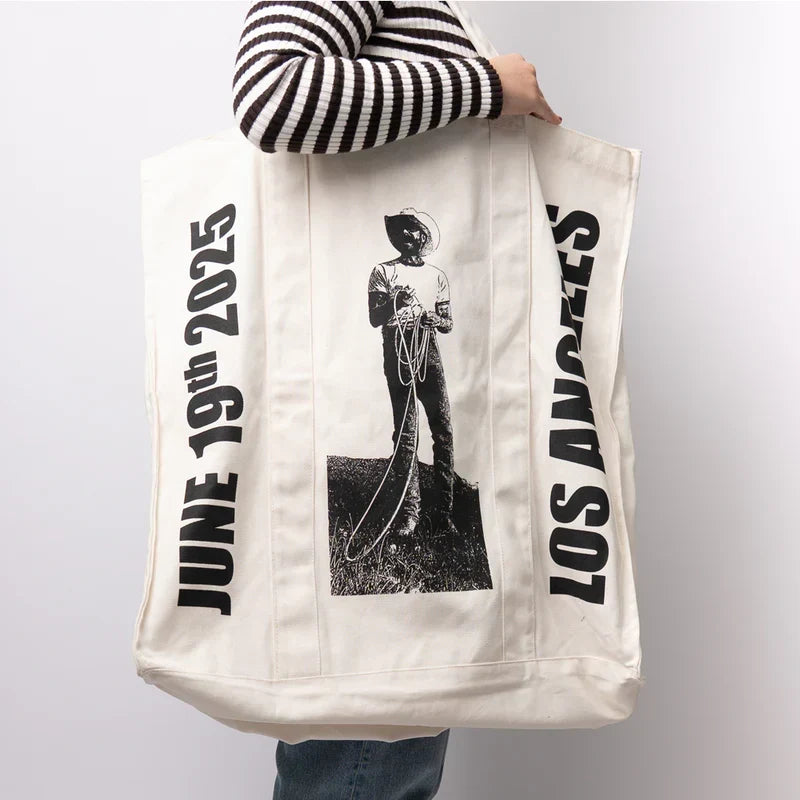 Model carrying the natural canvas Post Malone LA tour tote with cowboy statue photo and side lettering