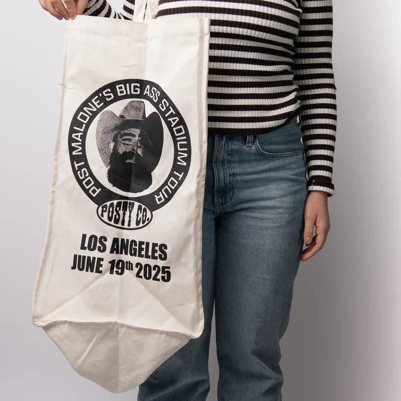 Natural canvas Post Malone LA tour tote with a circular Posty Co portrait badge held by a model
